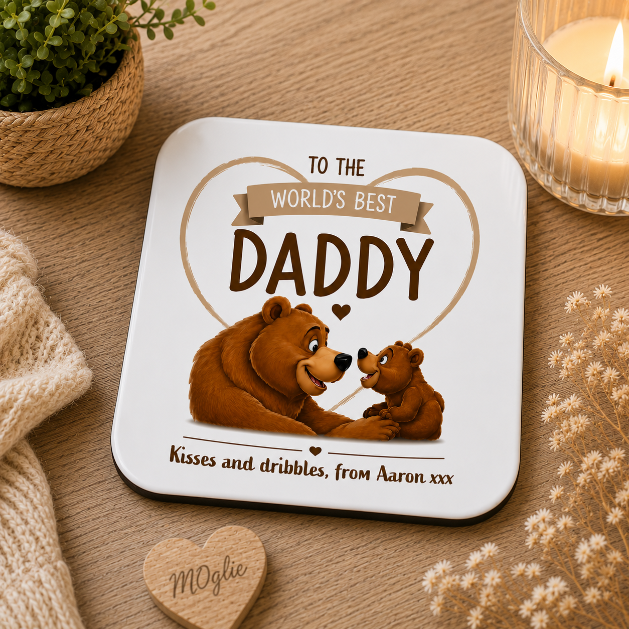 Coaster with bear design and text 'To the world's best daddy' on a wooden surface with a candle and plant.