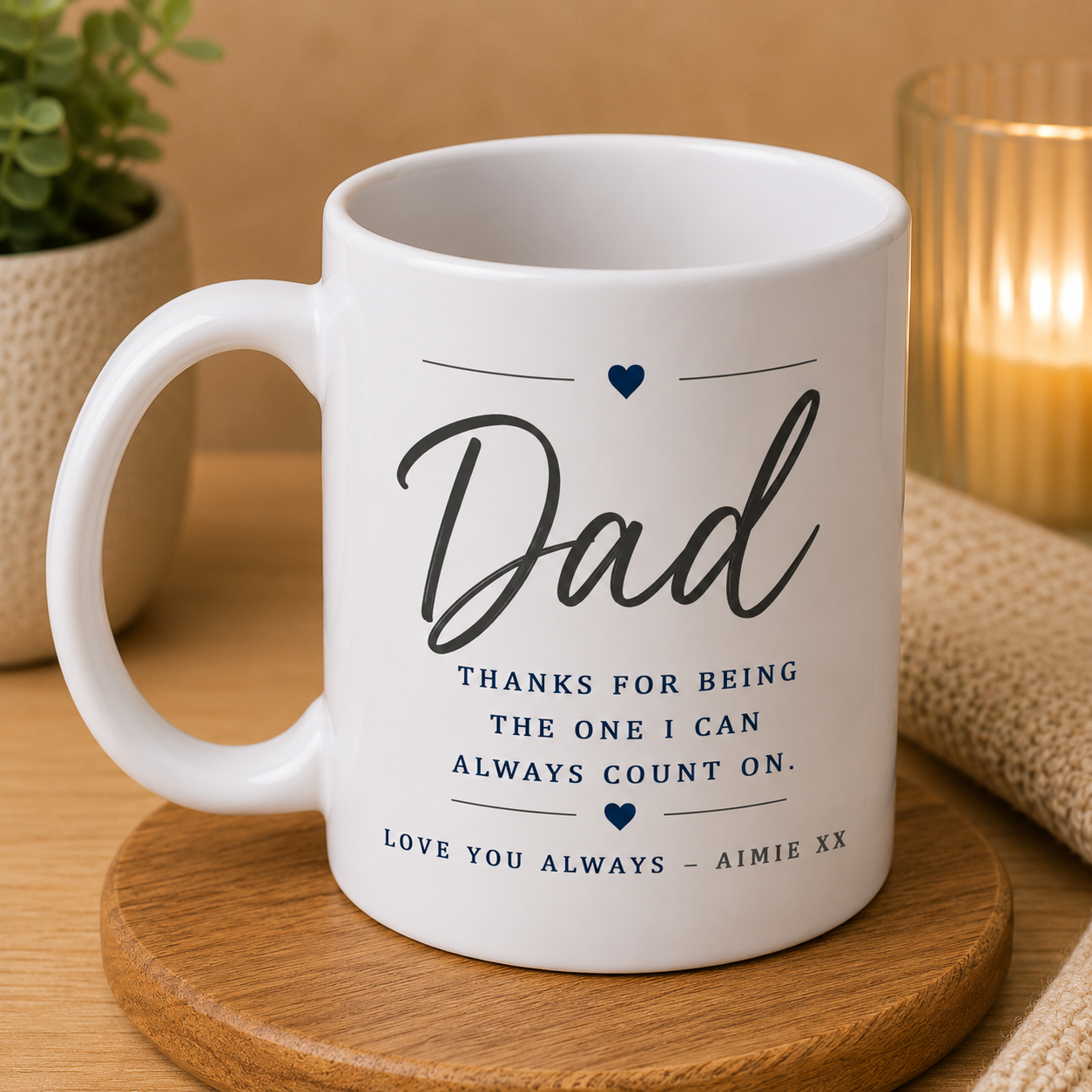 White mug with 'Dad' text on a wooden coaster with a candle and plant in the background