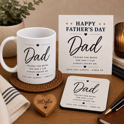 White mug with 'Dad' text, Father's Day card, coaster, and wooden heart on a wooden surface.